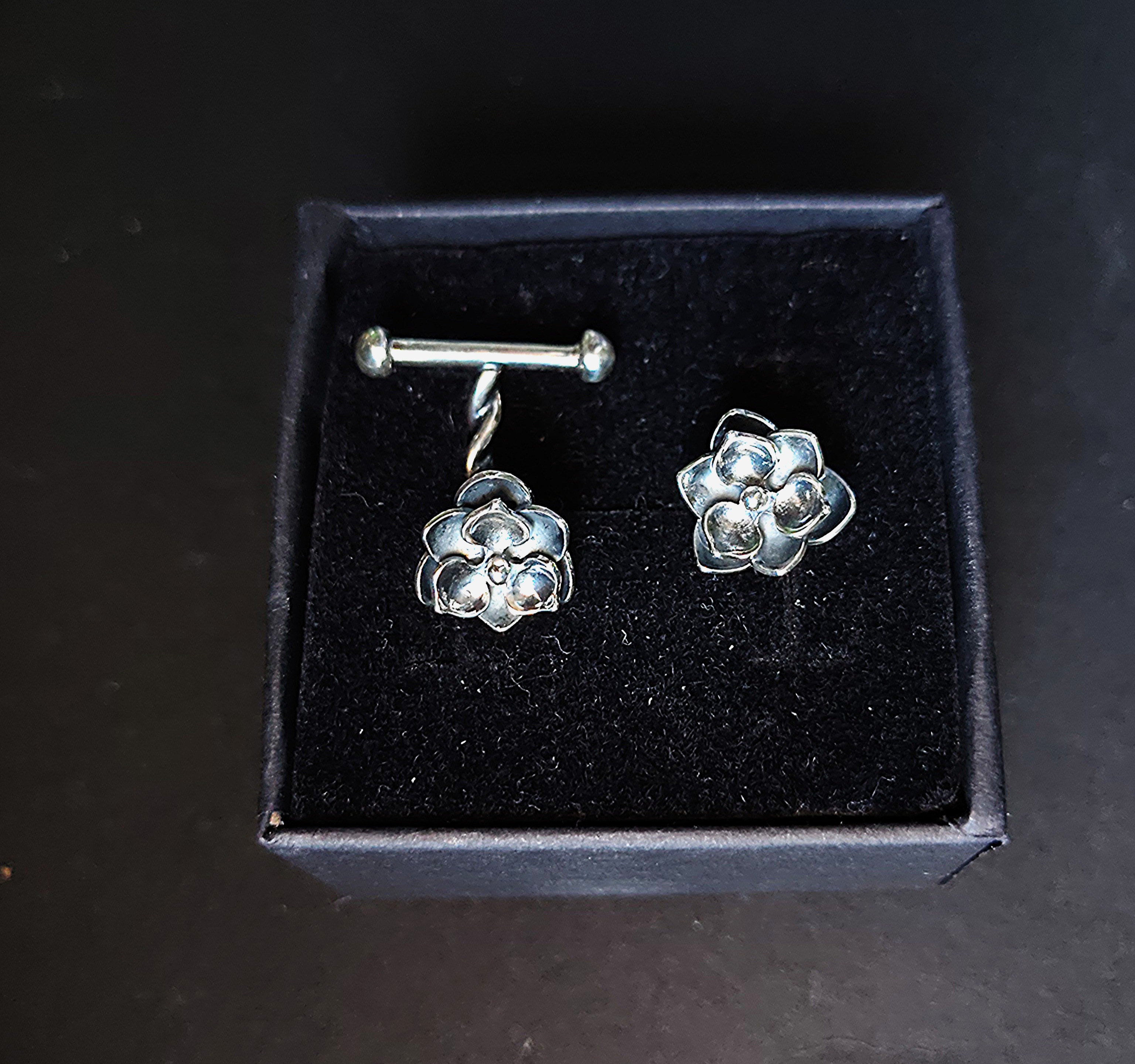 a pair of silver cufflinks with a magnolia flower